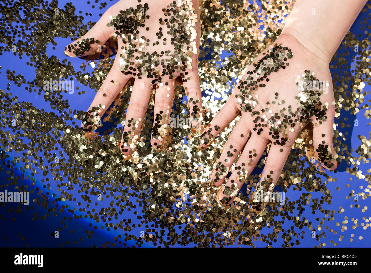 Hands of a child in gold glittering confetti on a blue background, top view. Birthday and holiday Stock Photo