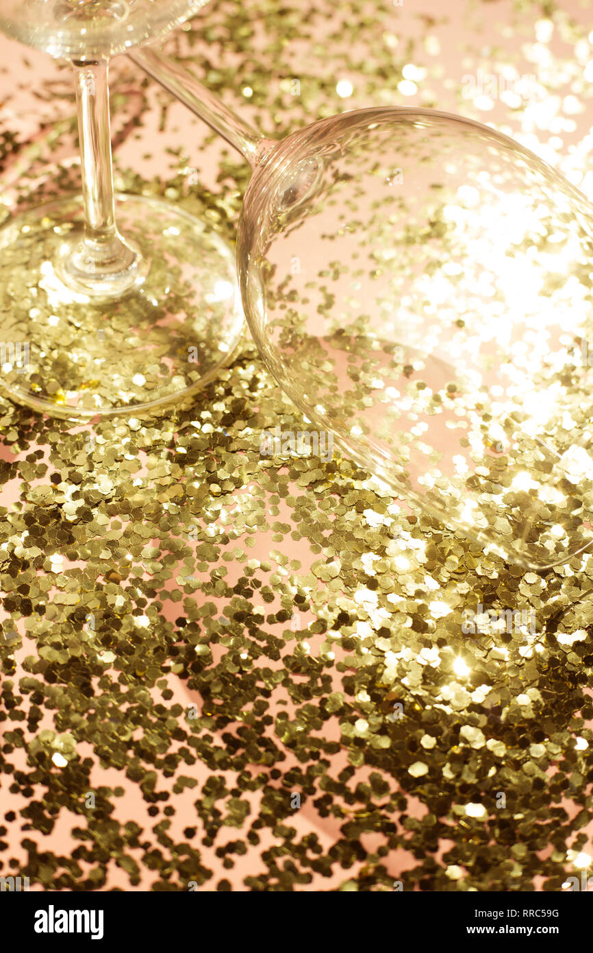 Empty glass goblets for champagne in golden confetti on the table. Festive background. Party concept Stock Photo
