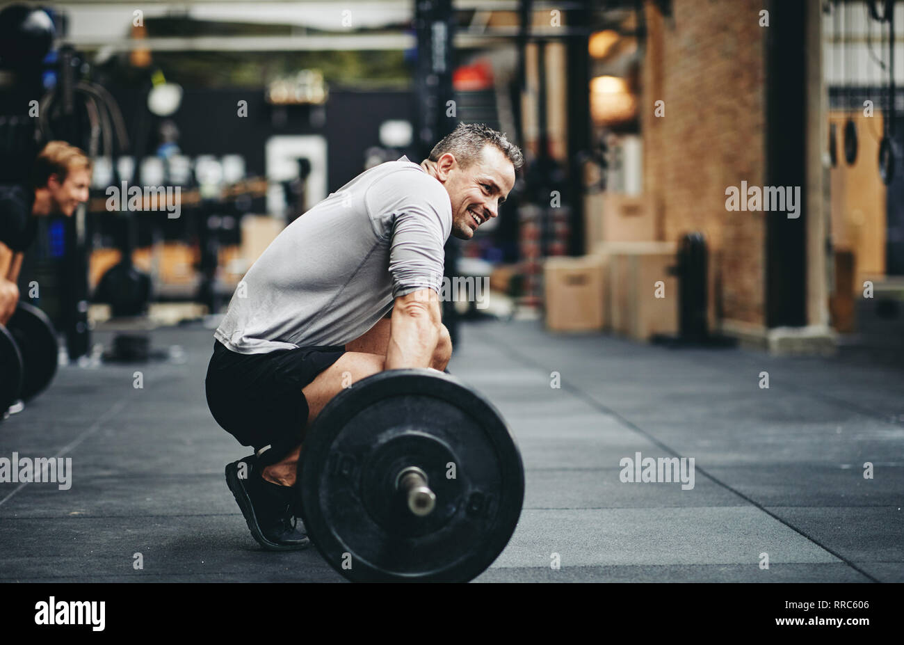 Fit man in sportswear smiling while preparing to lift heavy weights during a workout session at the gym Stock Photo
