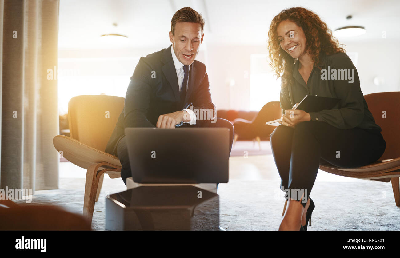 Two diverse young businesspeople discussing work and using a laptop while sitting together in a modern office Stock Photo