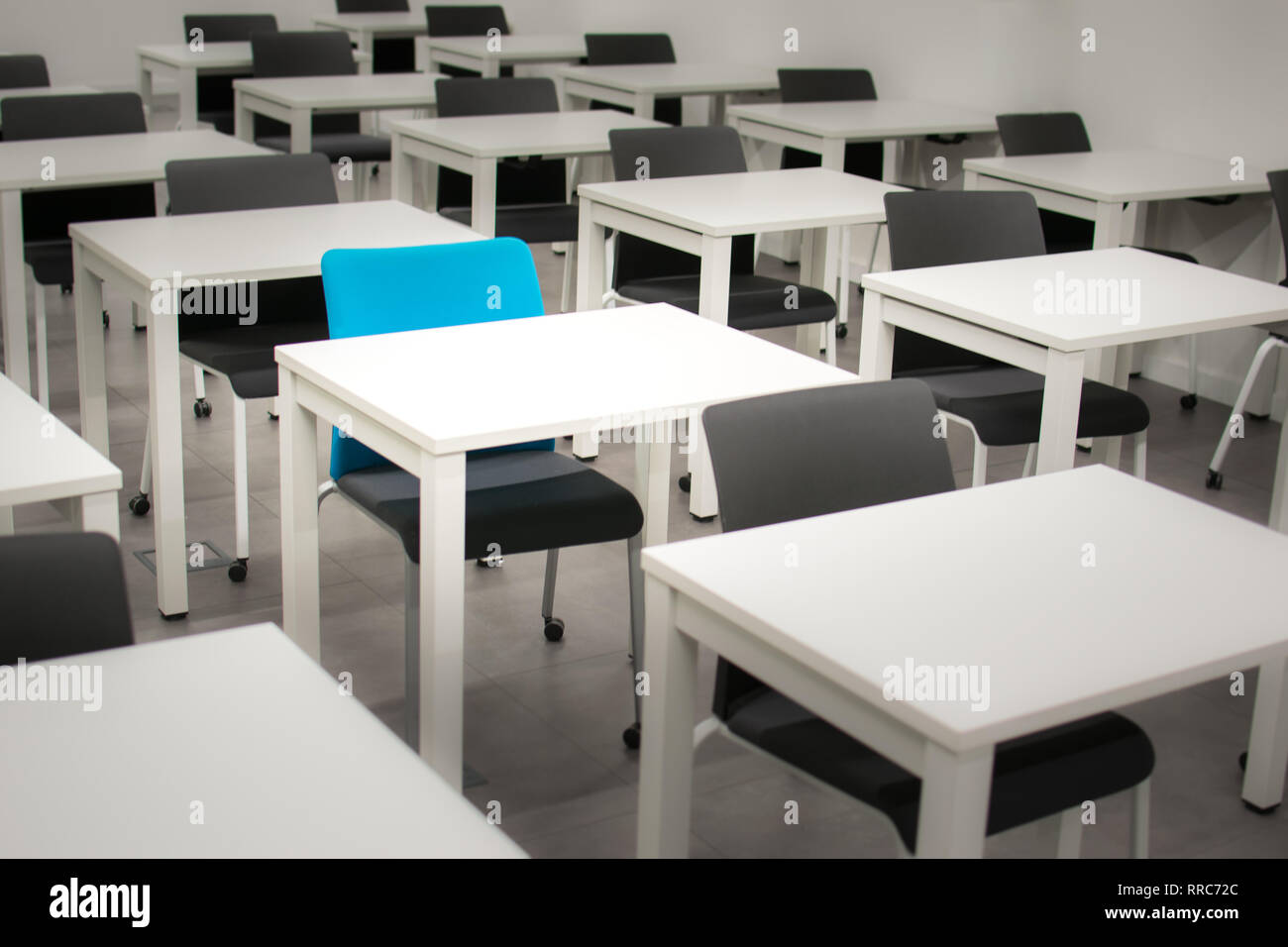 Classroom with black chairs and one blue chair. Hiring, vacant or choosing concept. White desks or tables Stock Photo