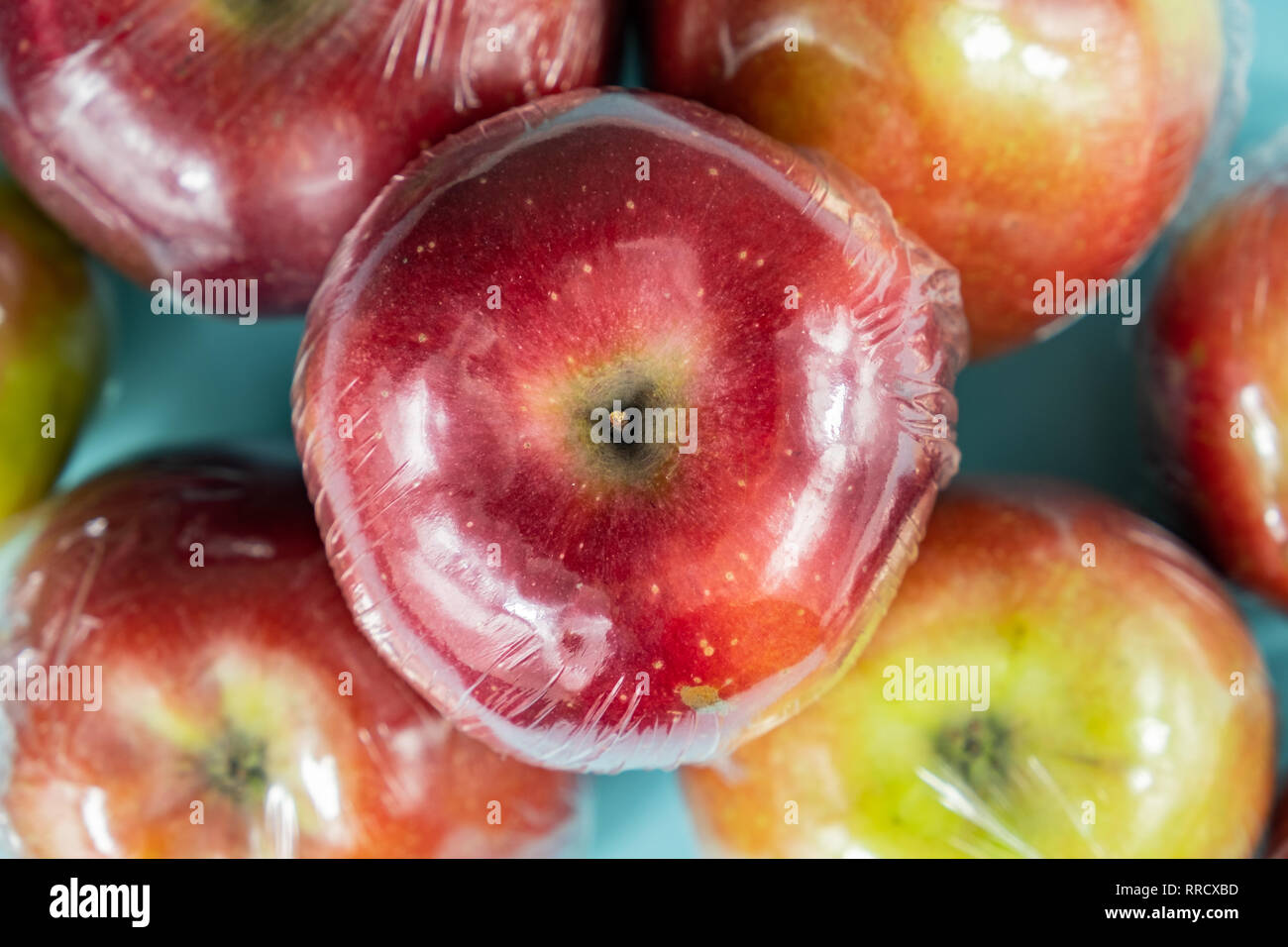 Excessive plastic use concept: fresh apples in kitchen wrap. Unreasonably over-packaged food products: fresh fruit in plastic wrap, close-up view Stock Photo