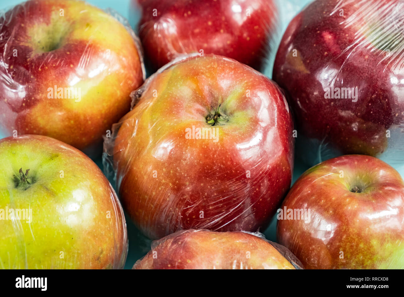 Excessive plastic use concept: fresh apples in kitchen wrap. Unreasonably over-packaged food products: fresh fruit in plastic wrap, close-up view Stock Photo
