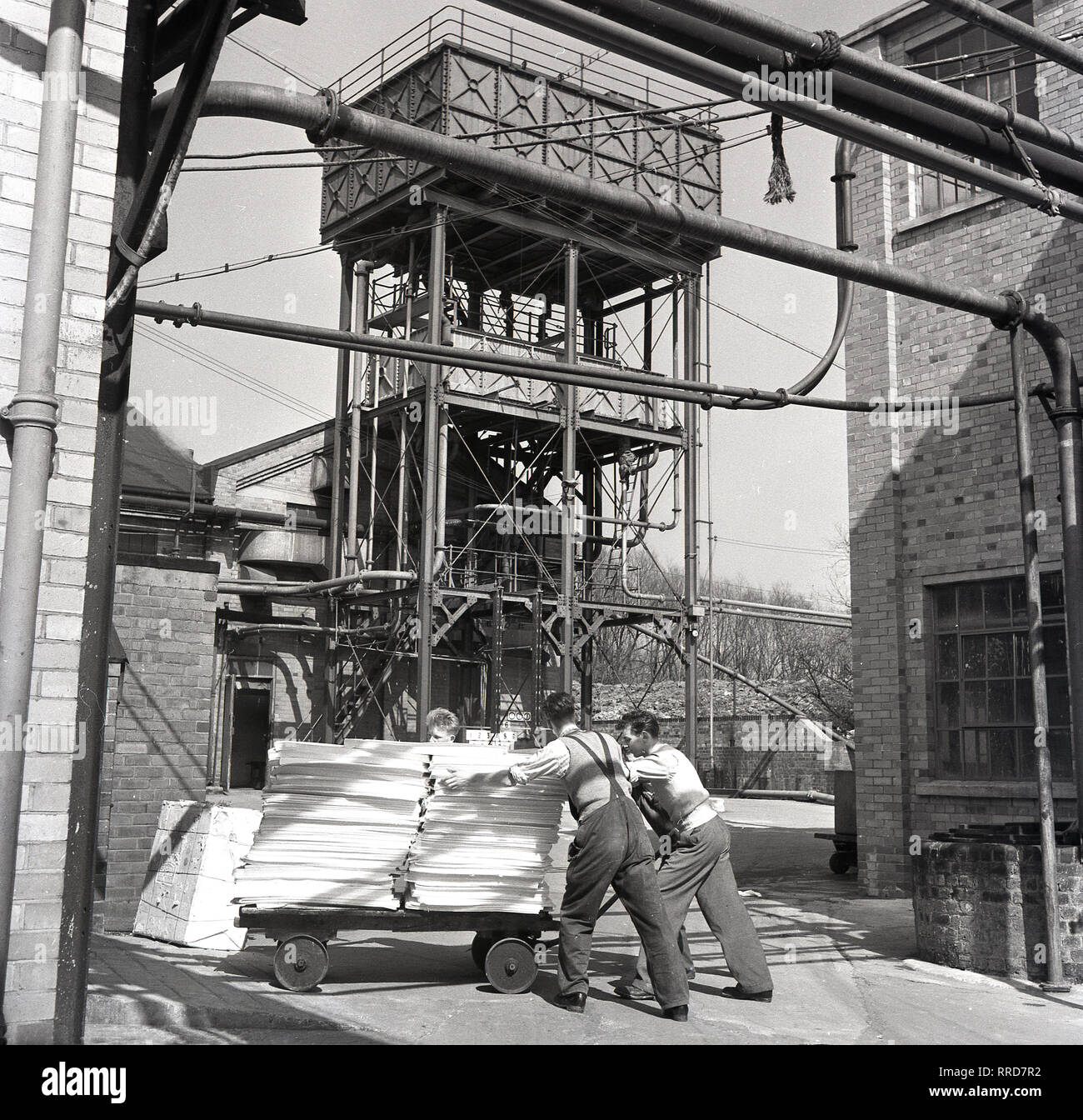 1950s, two male workers moving a trolley of finished paper outside a print works at the Brittains Paper Mill, England, UK. Stock Photo