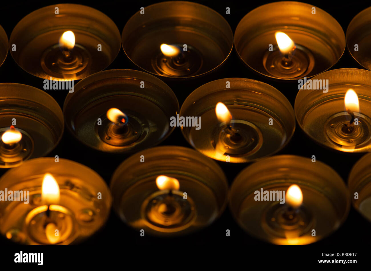 Many beautiful lit candles in a row glowing with a golden yellow light selective focus Stock