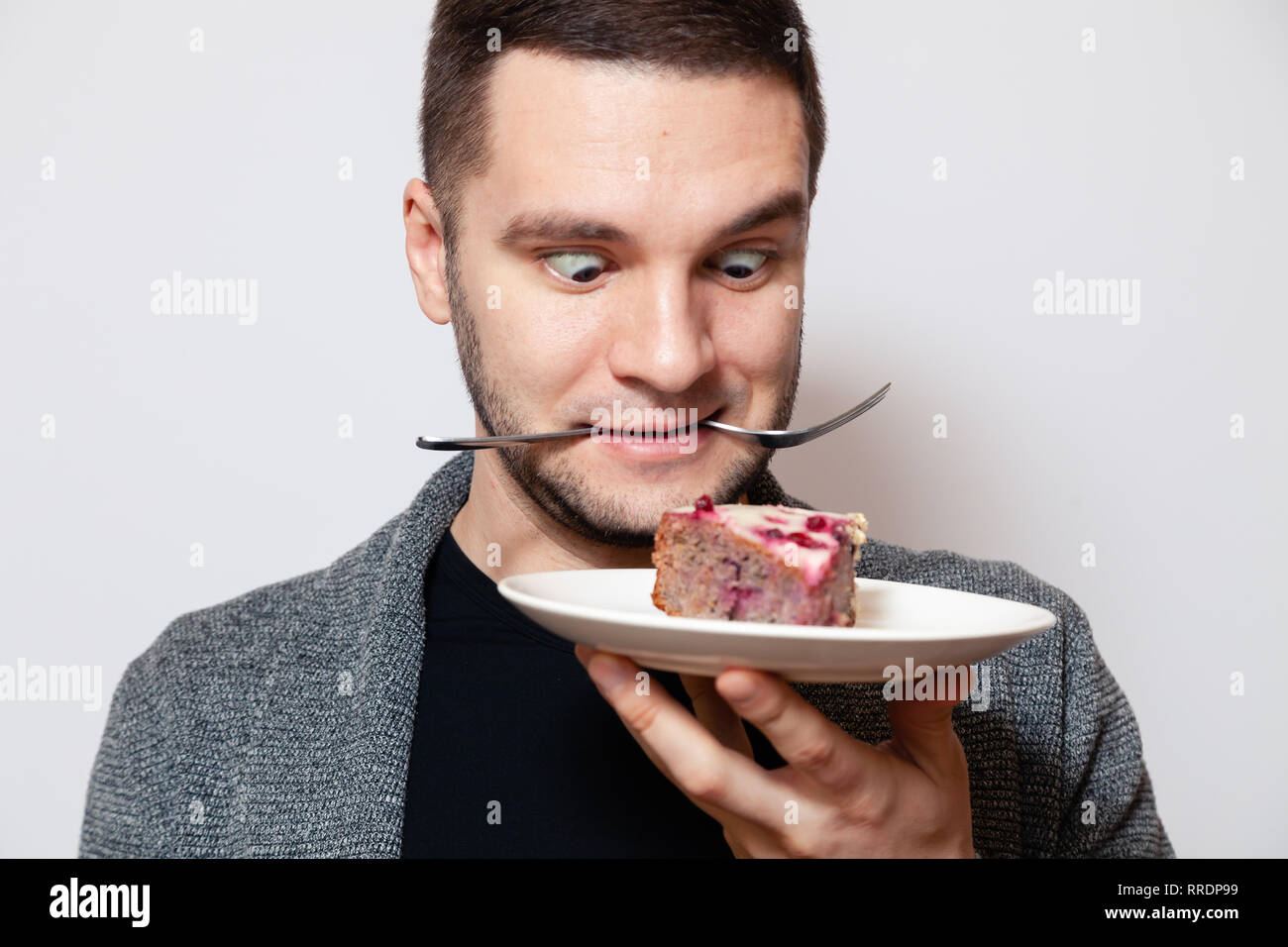 Closeup portrait young cute caucasian man smile, hold fork in his teeth and white round plate