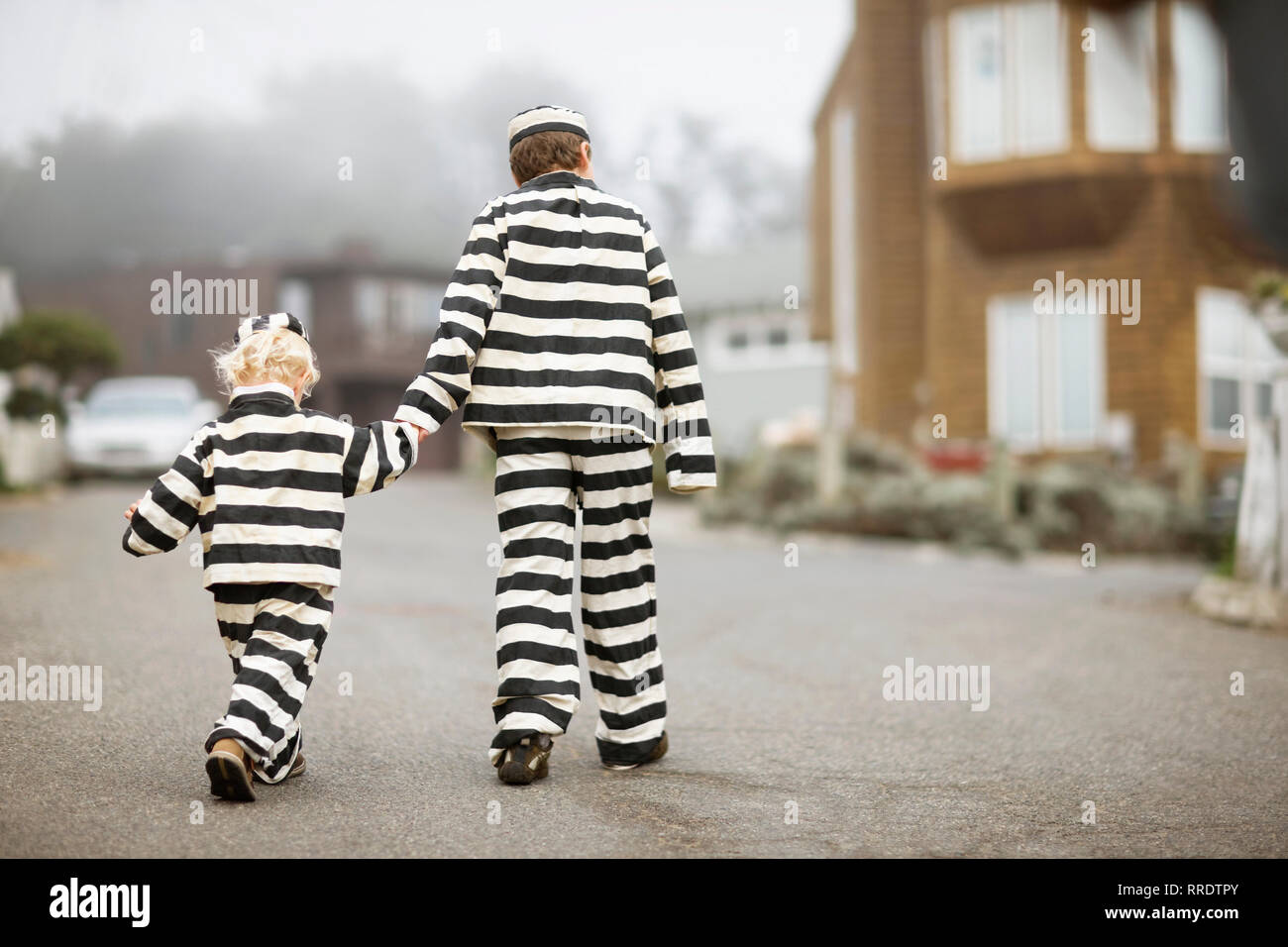 Boy holding hands with his younger brother,  both wearing prisoner costumes Stock Photo