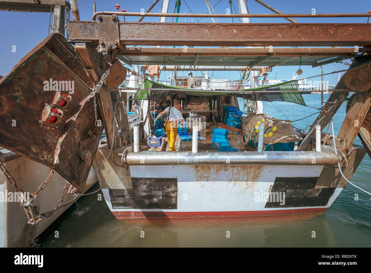 A fisherman wearing yellow overalls tidies up equipment on the deck of a fishing trawler at the port in Denia, Spain. Stock Photo