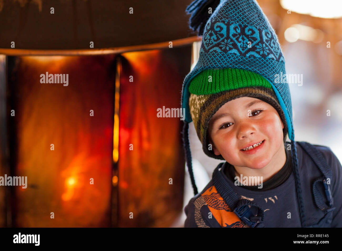 Portrait of a smiling young boy wearing three knitted hats inside a cabin. Stock Photo