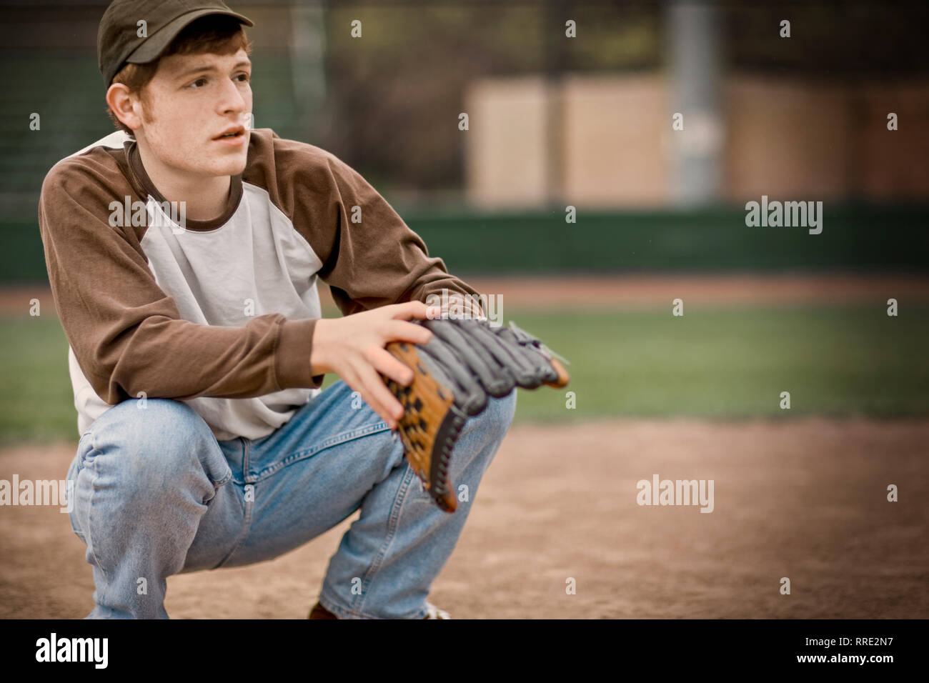 Teenage boy crouching with a baseball mitt on a sports field. Stock Photo