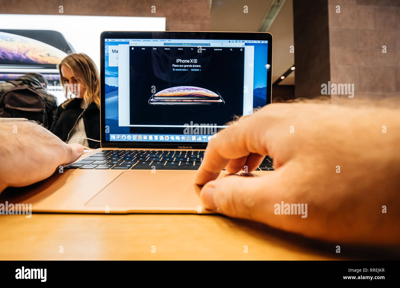 PARIS, FRANCE - NOV 8, 2018: Man hand touching the new Apple MacBook Air thin laptop featuring Retina screen and new CPU - reading website with iPhone XS Stock Photo