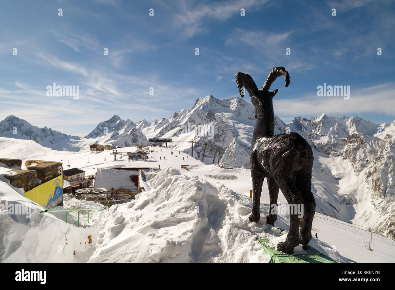 DOMBAI, RUSSIA, FEBRUARY 27, 2018: Monument to a mountain goat on the background of a ski lift and the high peaks of the Caucasus Mountains Stock Photo