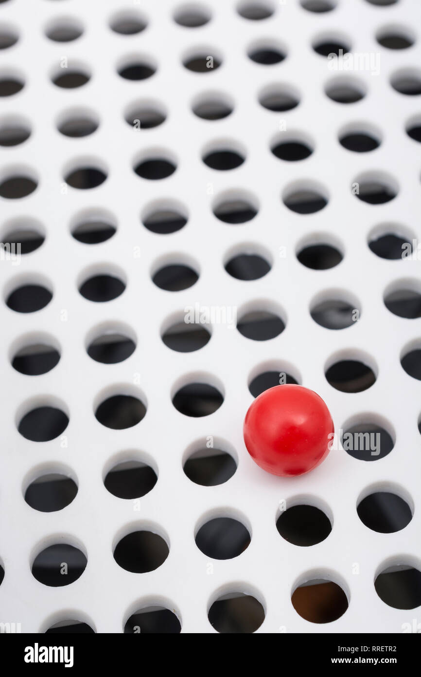 Abstract holes. Small solitary red plastic ball isolated on round holed