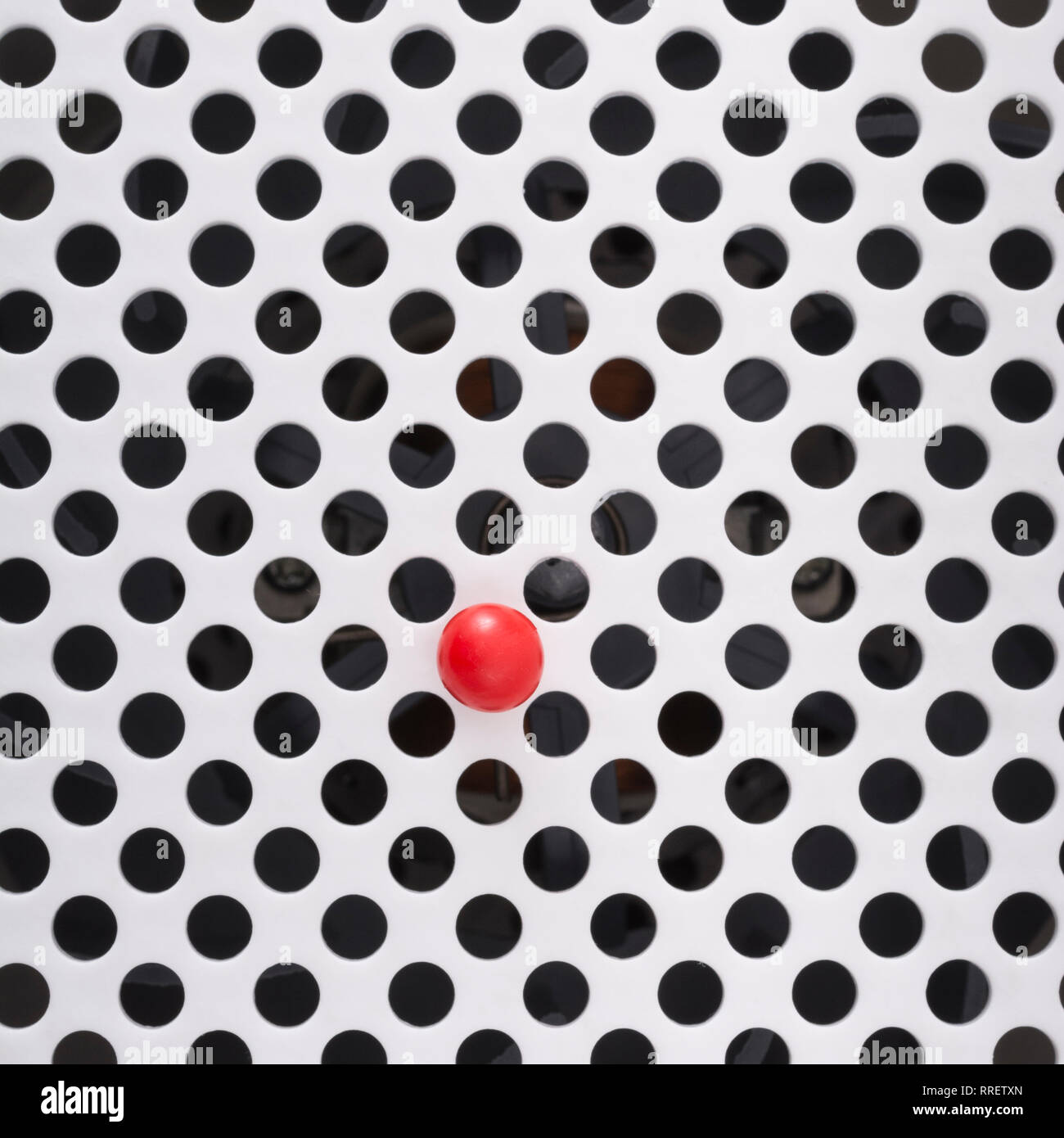 Abstract holes. Small solitary red plastic ball isolated on round holed