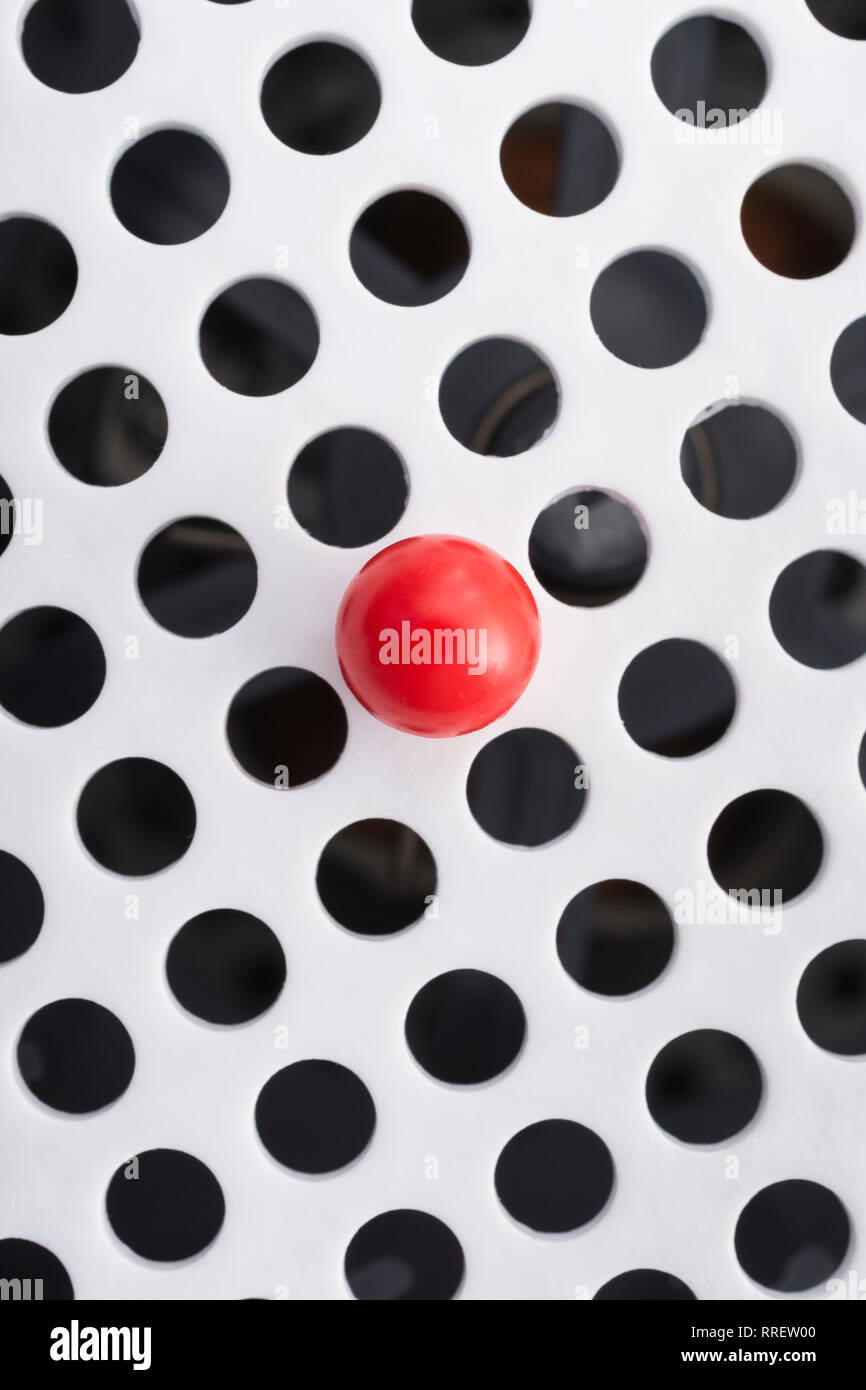 Abstract holes. Small solitary red plastic ball isolated on round holed