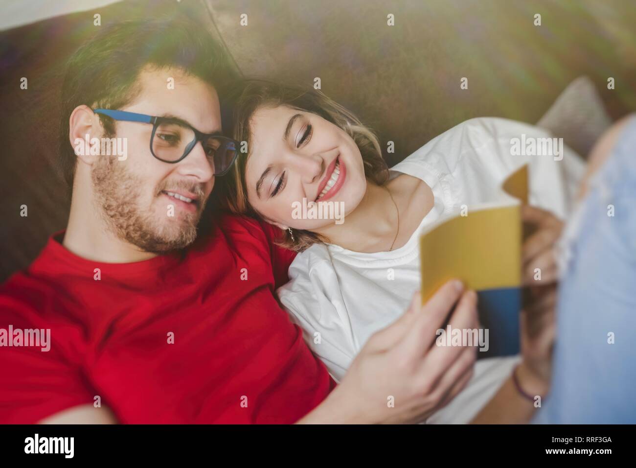 Cheerful dreamy man and Woman lying on couch and reading brochure Stock Photo