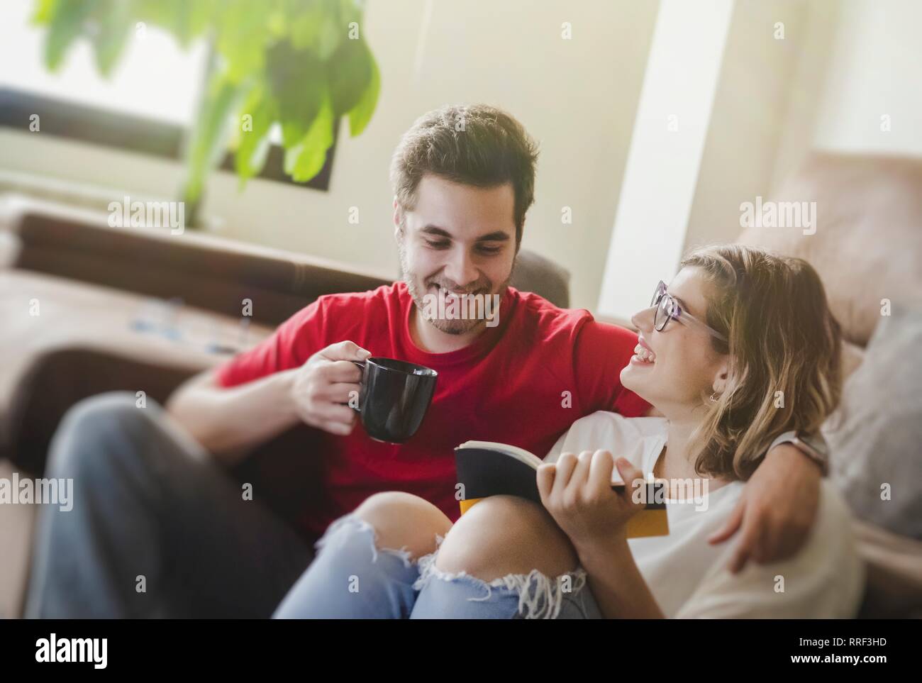 man drinking coffee while sitting on floor with girlfriend reading book Stock Photo