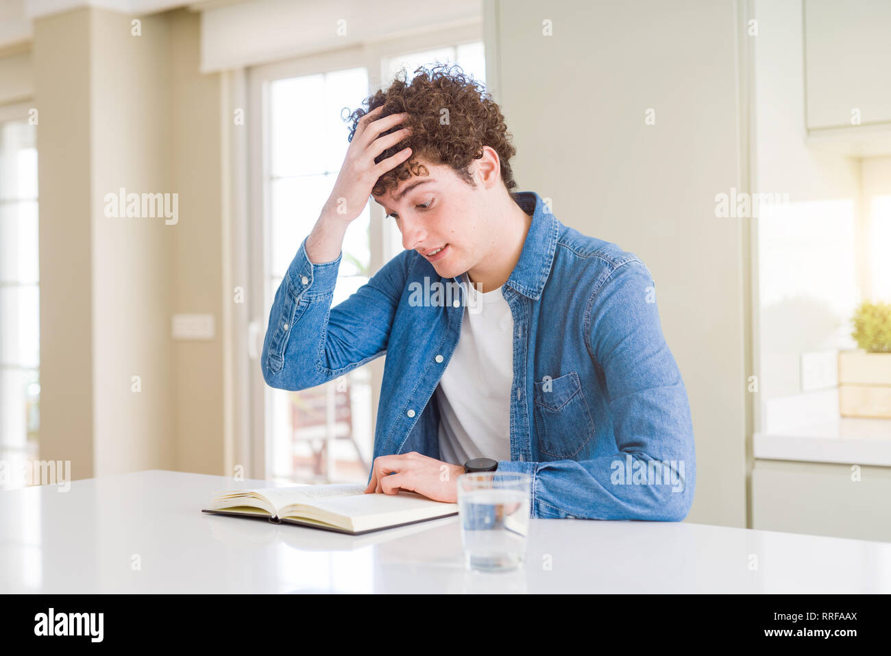 Young man reading a book at home stressed with hand on head, shocked with shame and surprise face, angry and frustrated. Fear and upset for mistake. Stock Photo