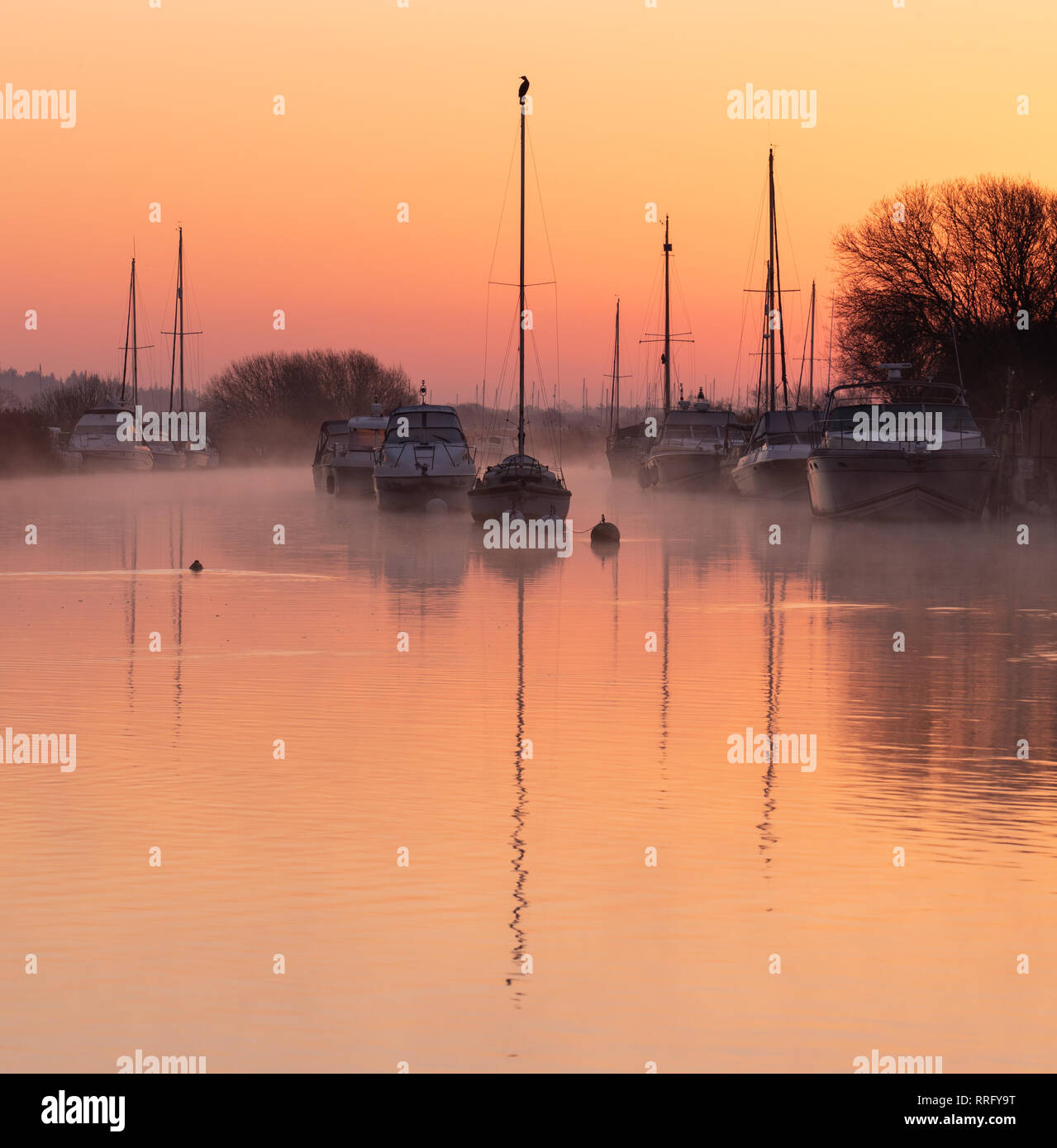 Wareham, Dorset, UK. 26th February 2019. UK Weather: The sky glows with orange and pink hues as the mist rises over the River Frome on a crisp, chilly February morning. A tranquil scene as sailing boats moored along the river bank are reflected in the calm water on the start of what is set to be another gloriously sunny day.  Credit: Celia McMahon/Alamy Live News Stock Photo