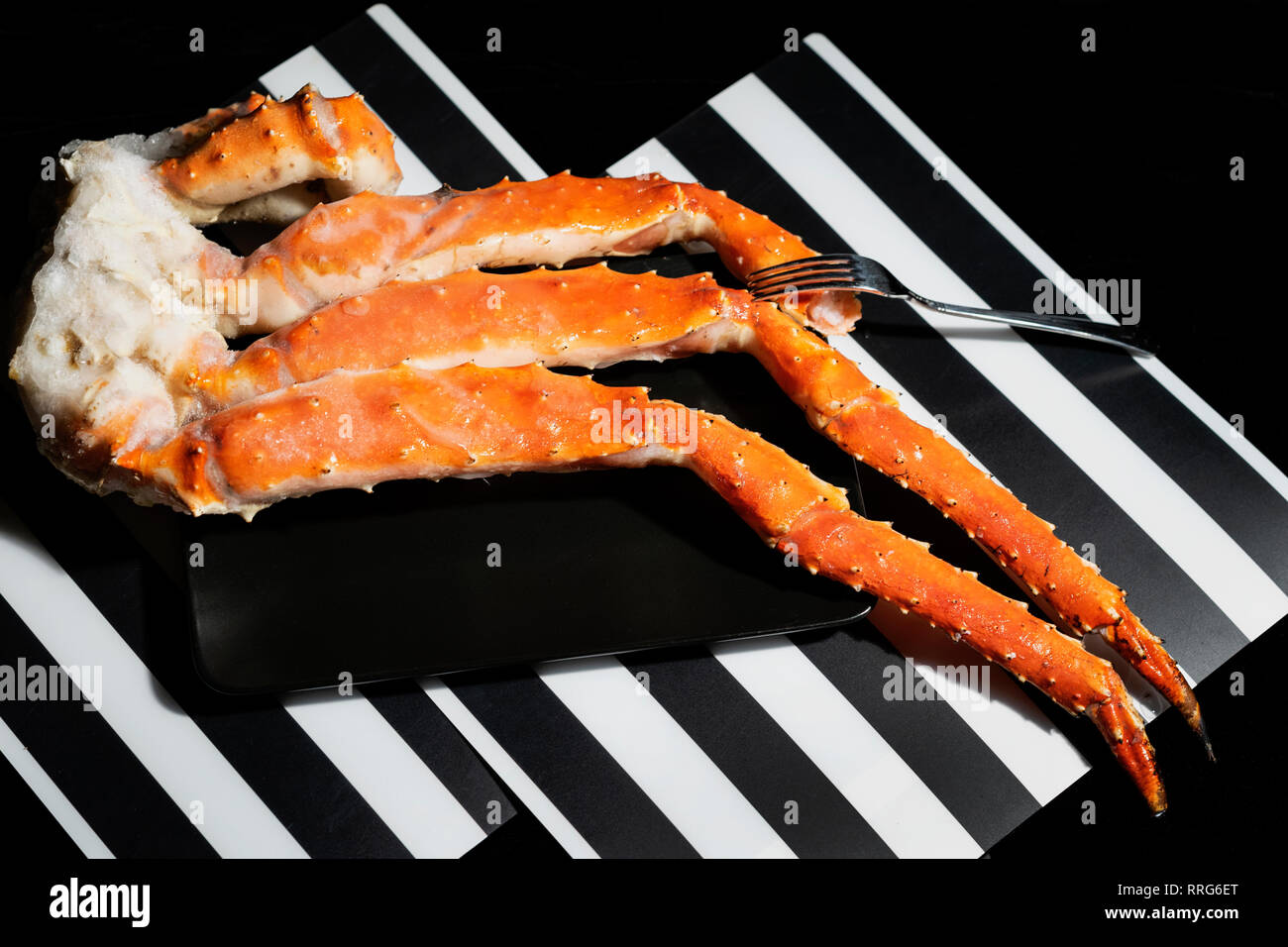 Crab legs and fork in black plate on black and white striped background