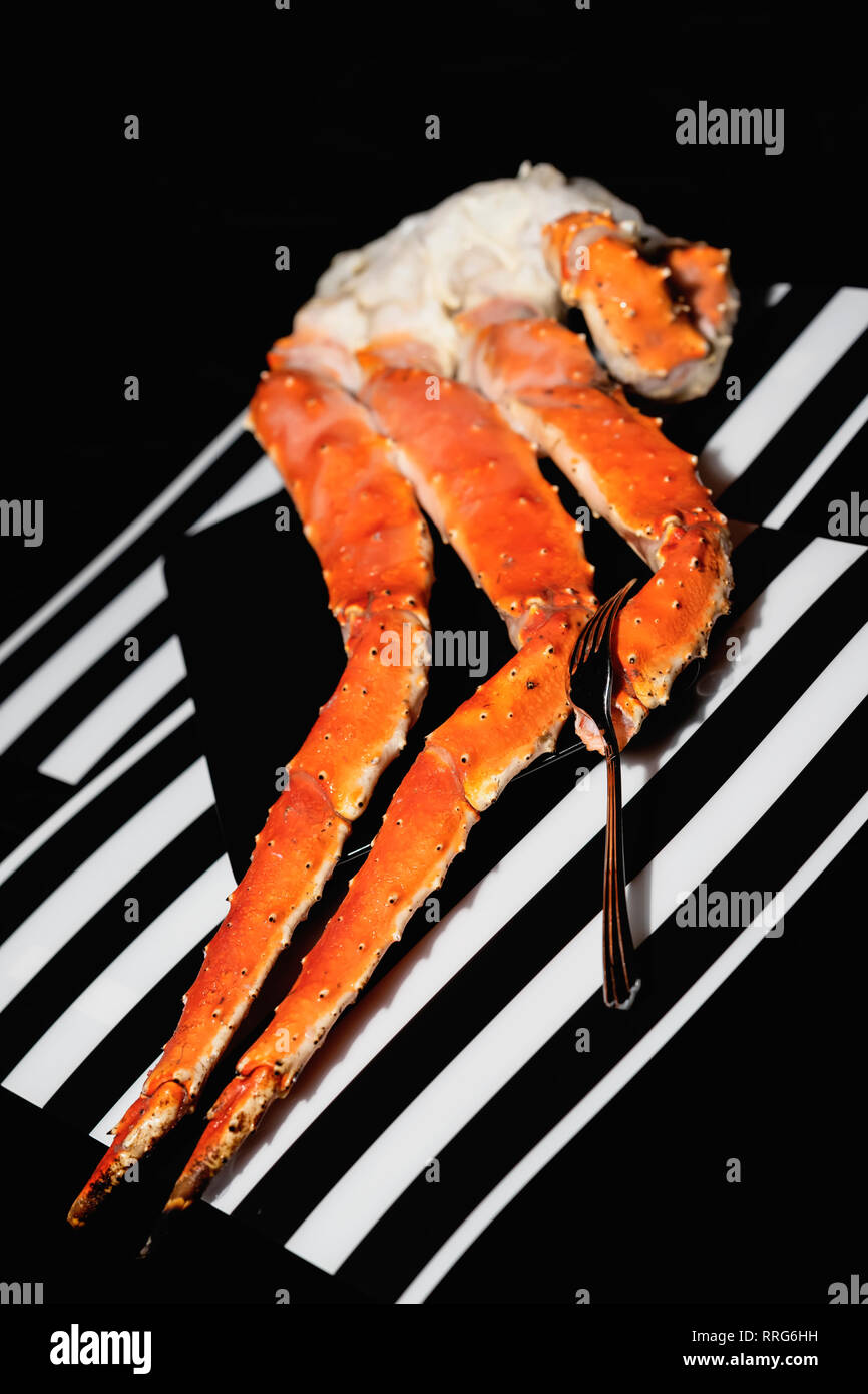 King crabs legs and fork in black plate on black and white striped