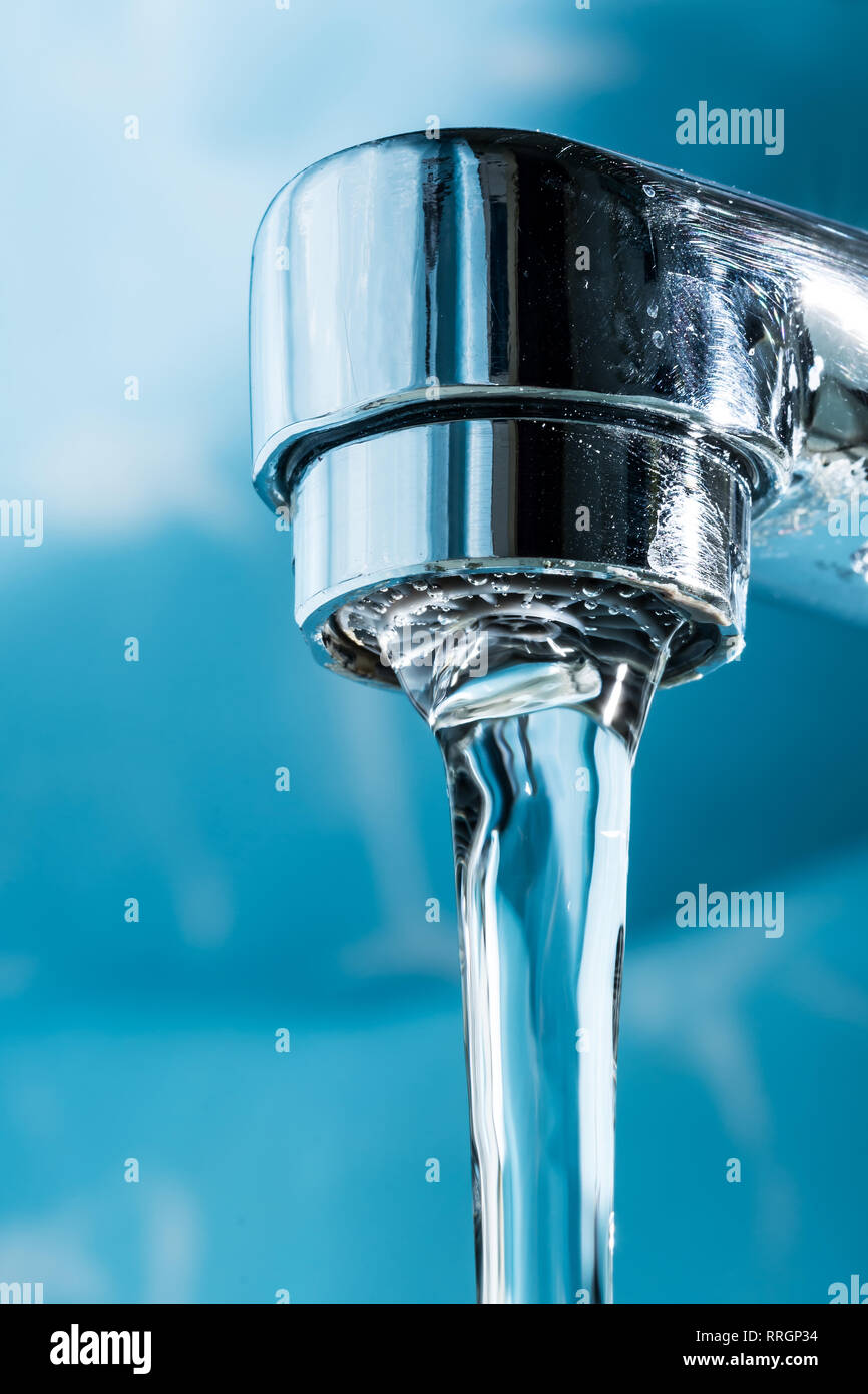 Water flows from a modern chromed water tap faucet macro close up