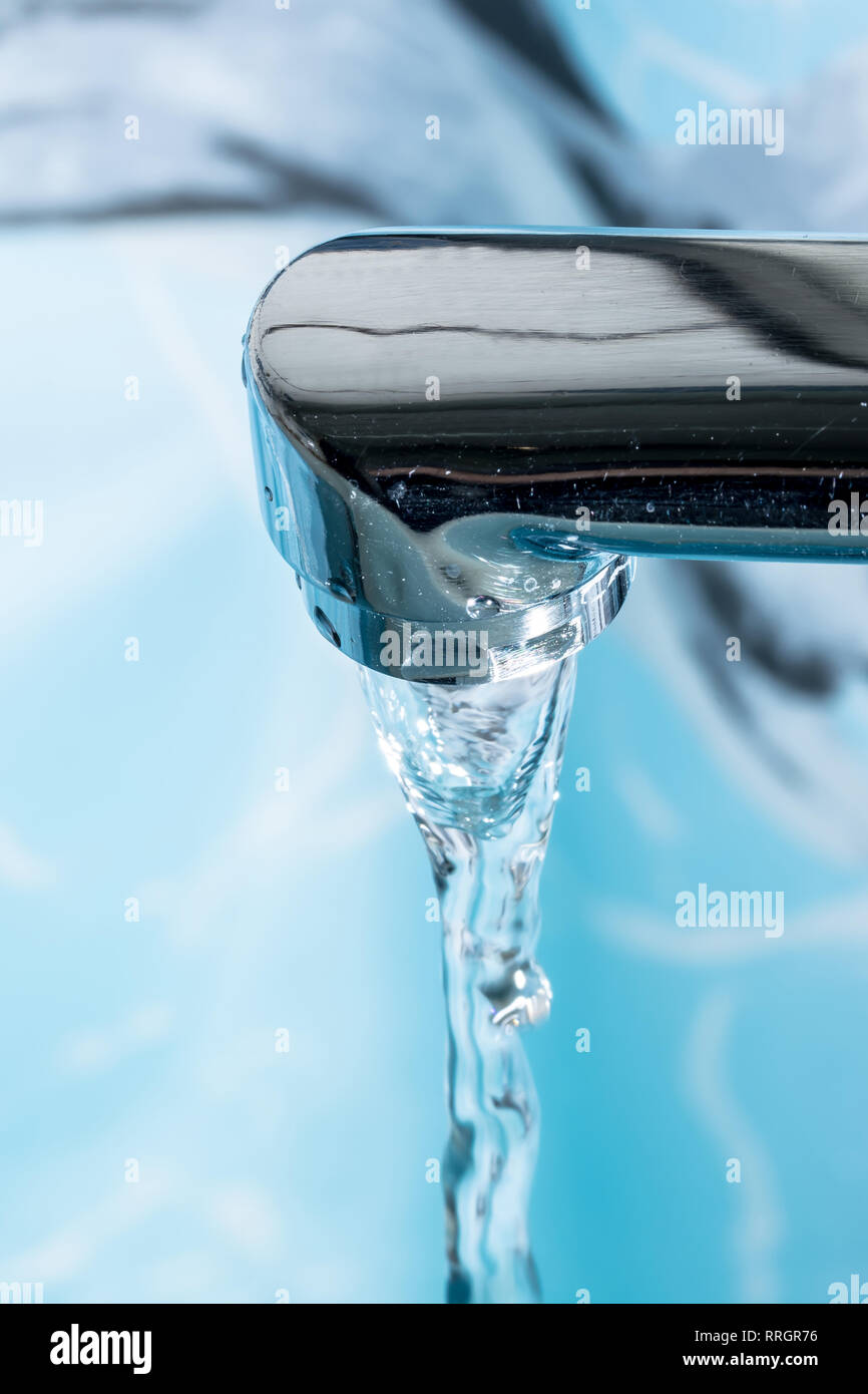 Water flows from a modern chromed water tap faucet macro close-up. Stock Photo
