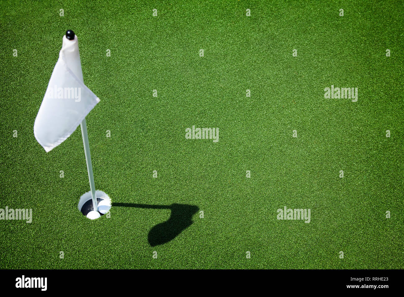 Two golf balls sit inside cup on golf course putting green with flag. Stock Photo