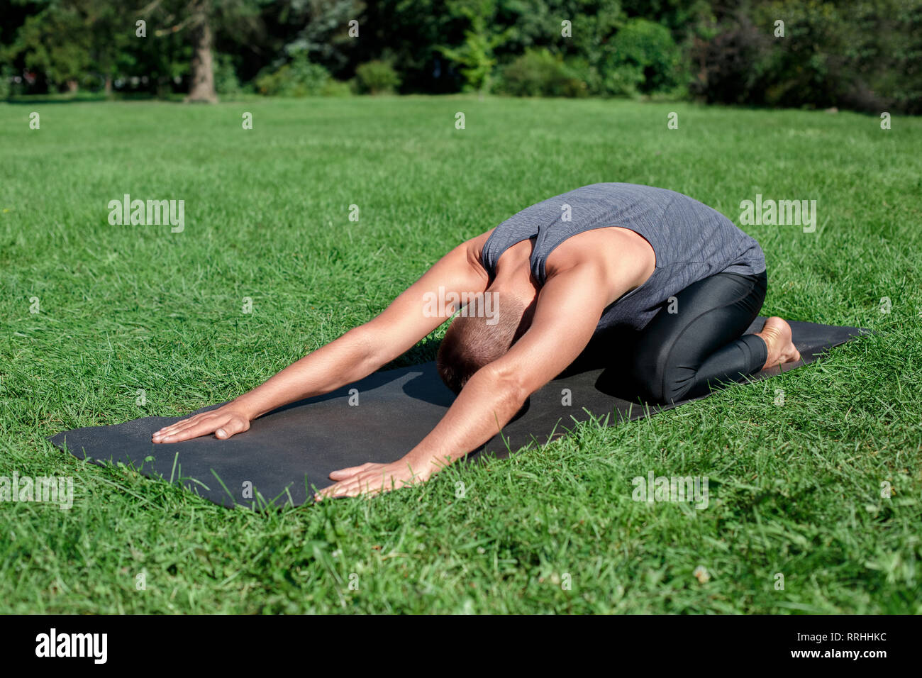 Healthy Lifestyle. Man practicing yoga on mat outdoors in child pose stretching back Stock Photo