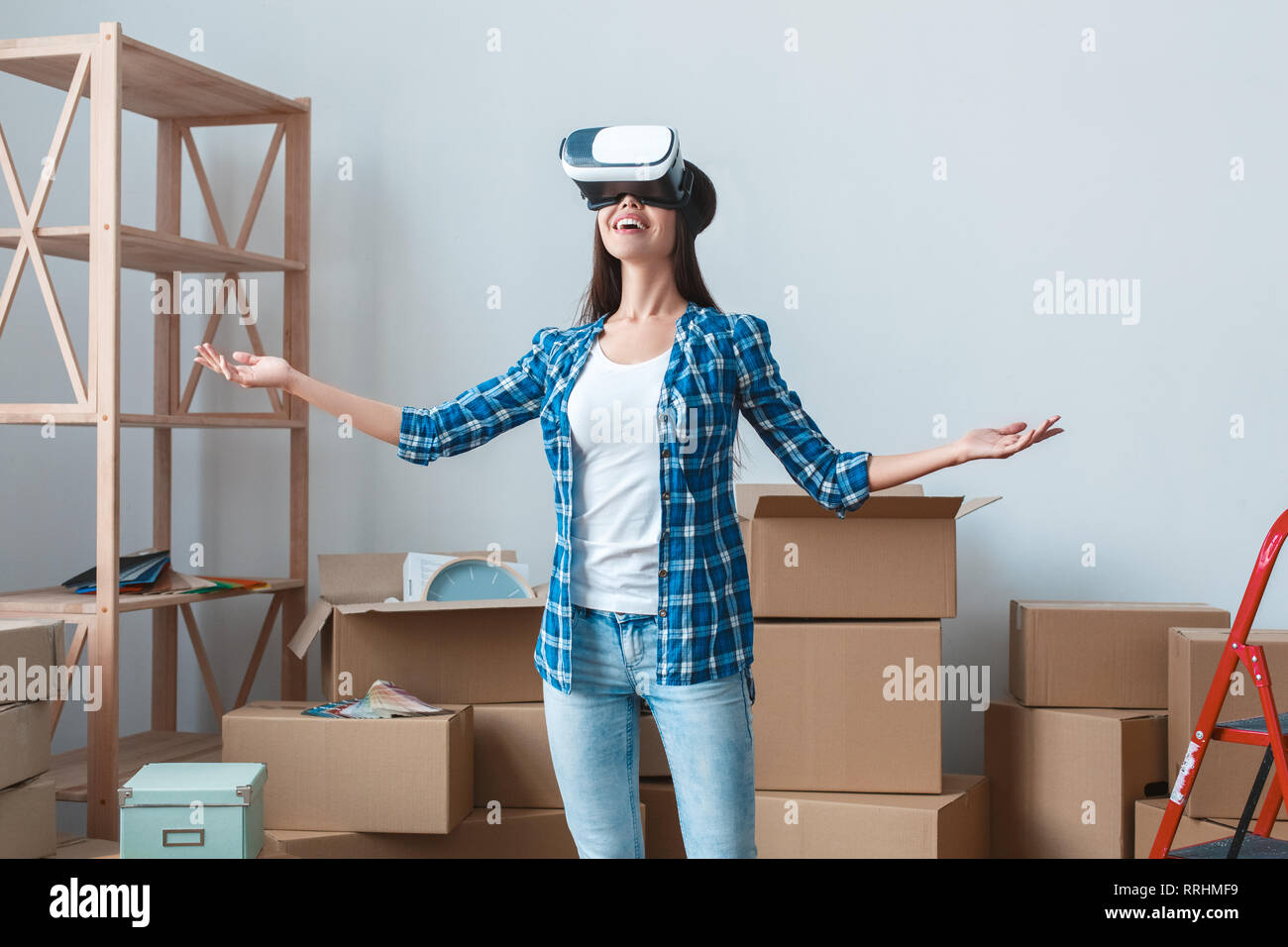 Young woman moving to a new place standing looking in virtual reality headset smiling excited Stock Photo