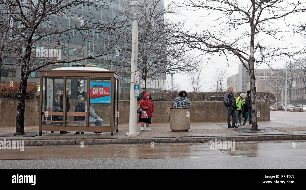 People wait in the rainy winter weather at a public bus stop in downtown Cleveland, Ohio, USA. Stock Photo