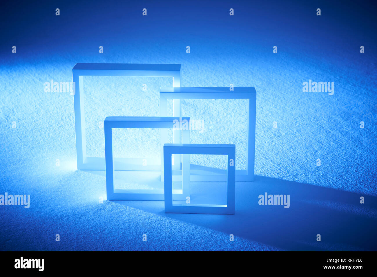 Four square white frames of various sizes sitting on a white surface toned with a blue background. Stock Photo
