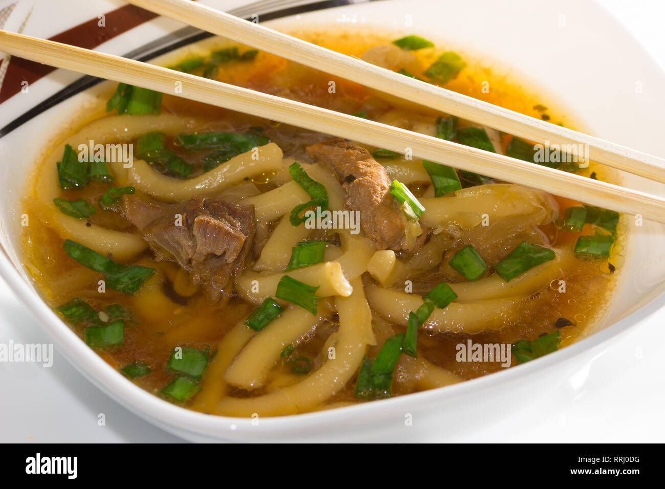 Bowl of miso soup with udon noodles, cabbage, pork and green onions with chopsticks on a bamboo napkin Stock Photo