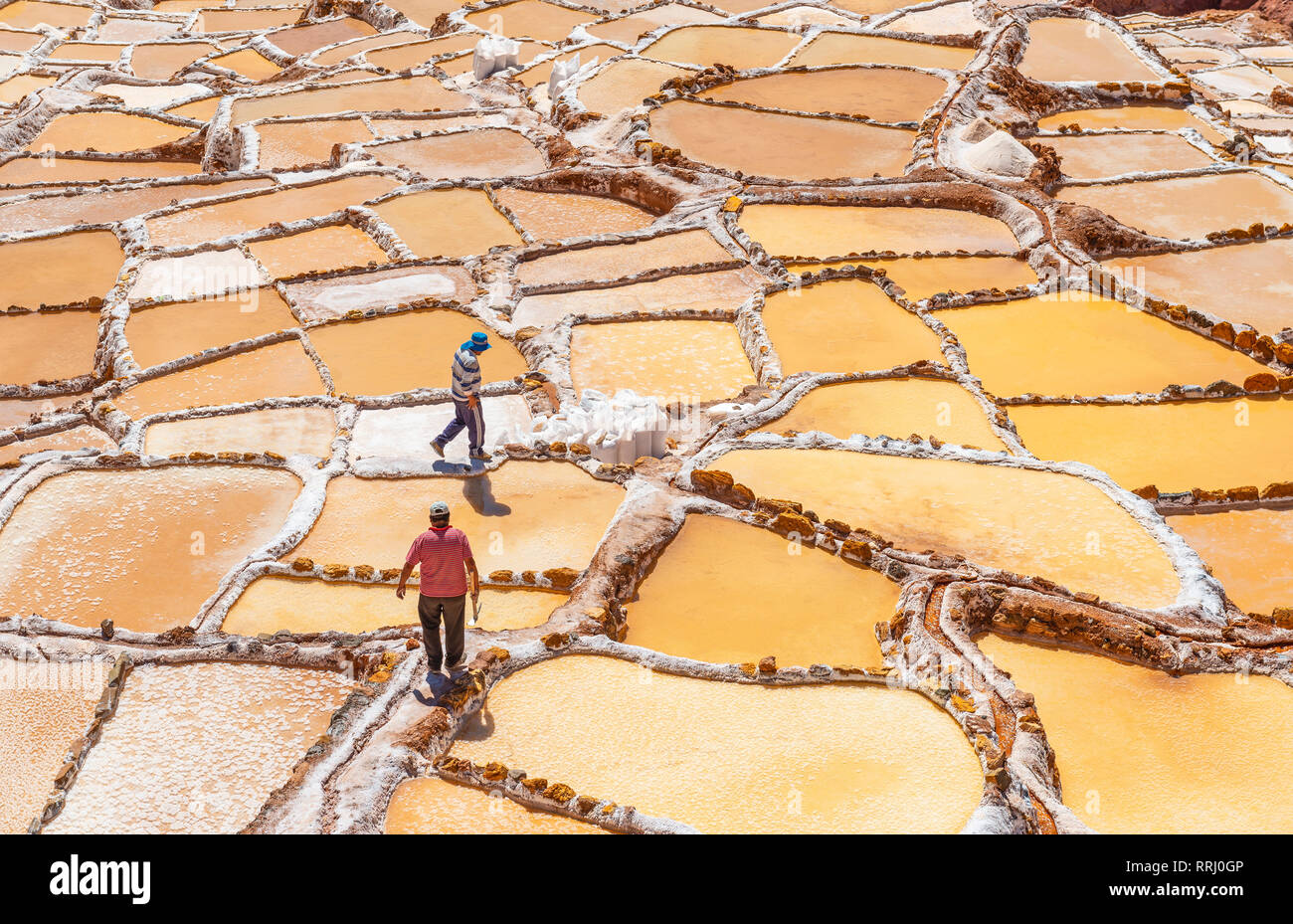 Two men at work collecting salt and salt bags in the famous salt terraces of Maras near the city of Cusco, Peru. Stock Photo