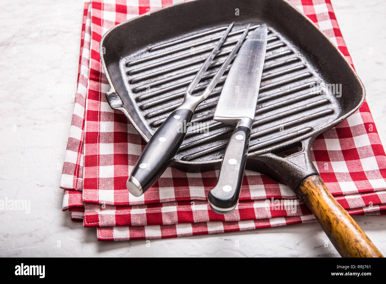 Empty grill pan on marble table with red tablecloth knife and fork. Stock Photo