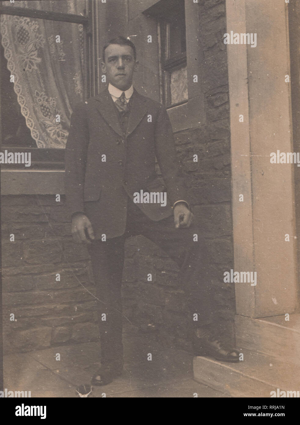 Vintage Edwardian Photographic Postcard Showing a Suited Man Stood Next To The Door of a House. Stock Photo