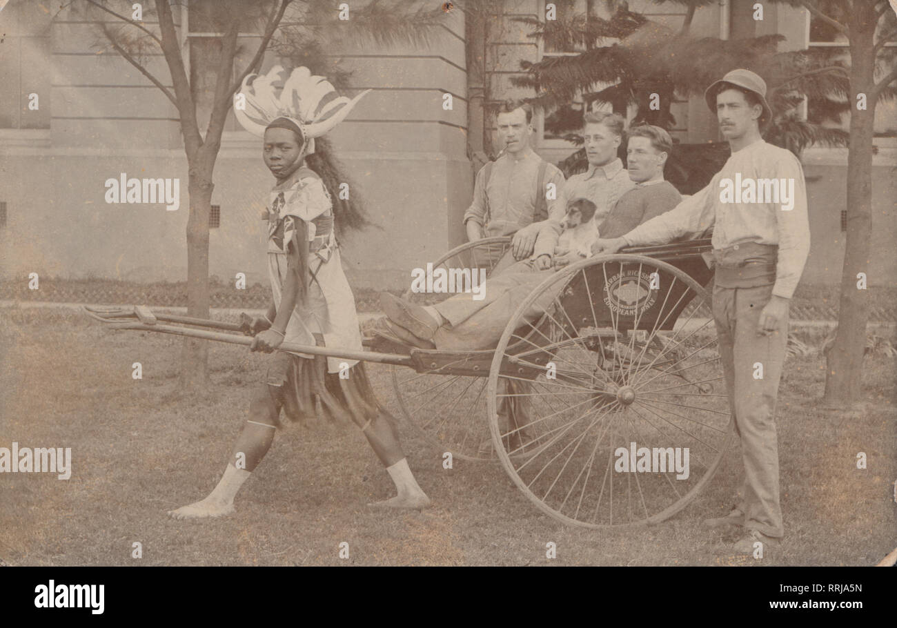 Vintage Photographic Postcard Showing White Men Being Given a Ride in a Rickshaw by a Black South African. Durban Ricksha Ltd, Europeans Only Written on The Side of The Carriage. Stock Photo
