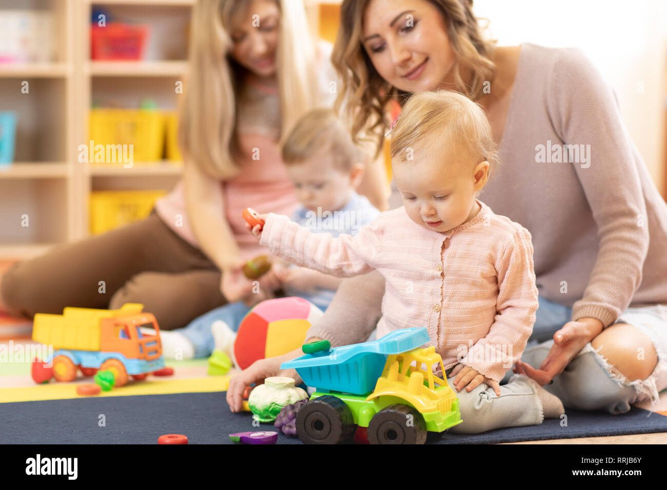 Nursery babies playing with adults in daycare center Stock Photo