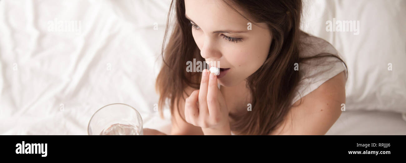 Closeup woman put pill in mouth holding glass with water Stock Photo