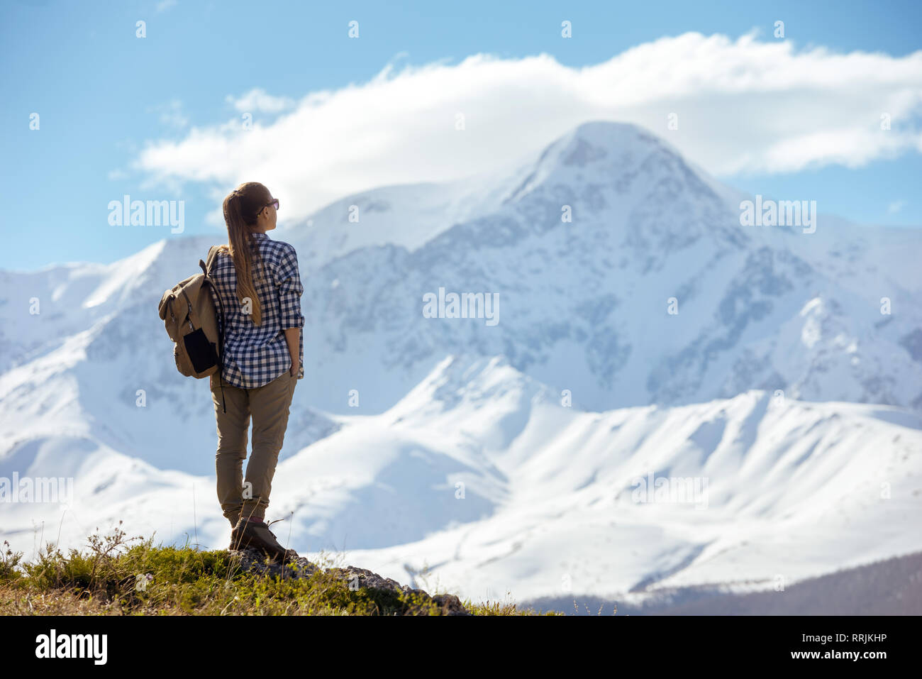 Woman with backpack stands on viewpoint and looks at mountains Stock Photo