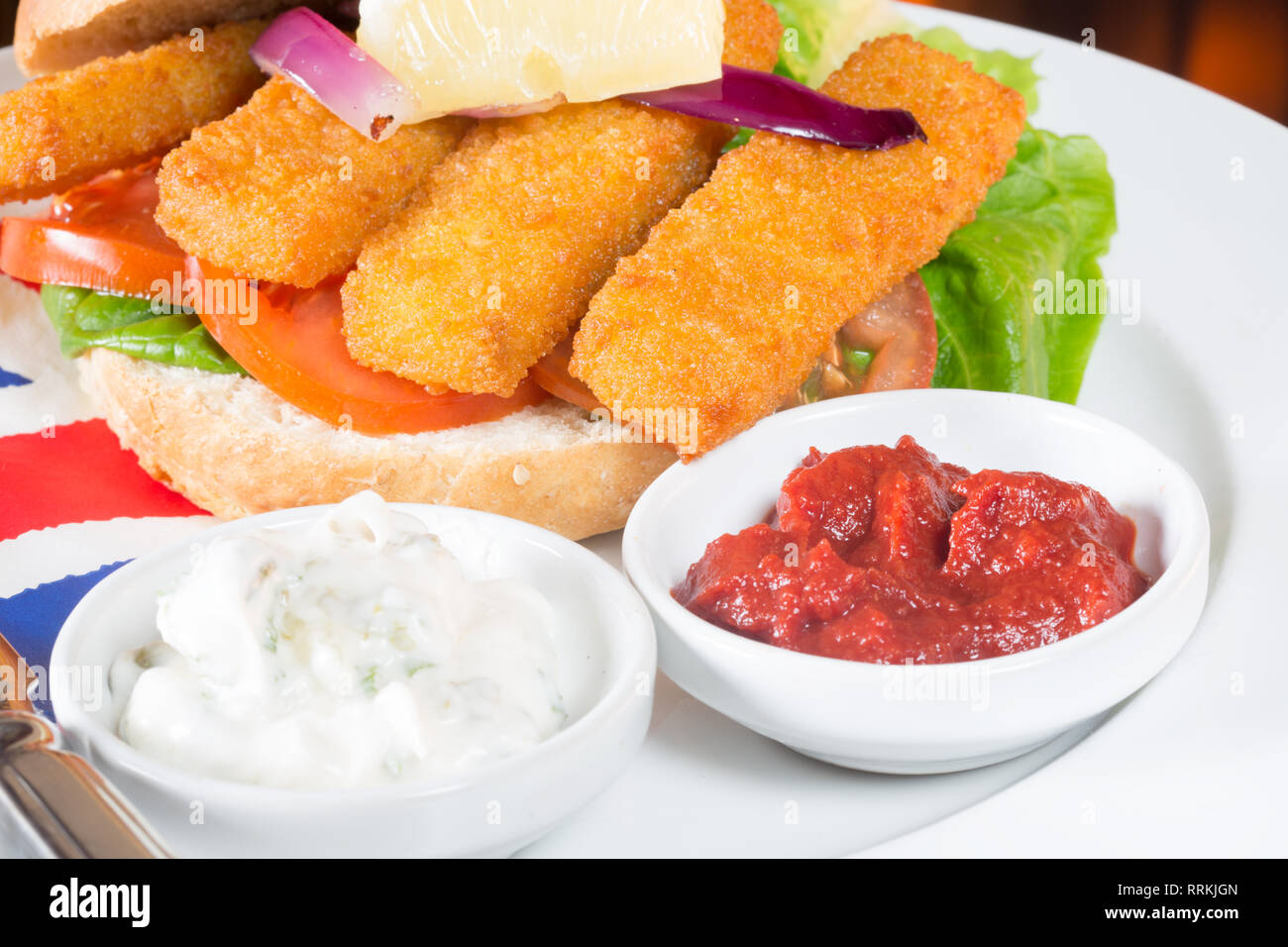 Typical English lunch snack of Fish fingers in a bun with ketchup and Tartar. Stock Photo