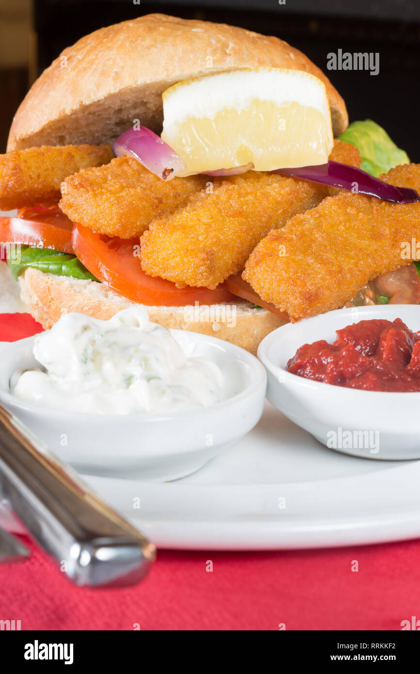 Typical English lunch snack of Fish fingers in a bun with ketchup and Tartar. Stock Photo