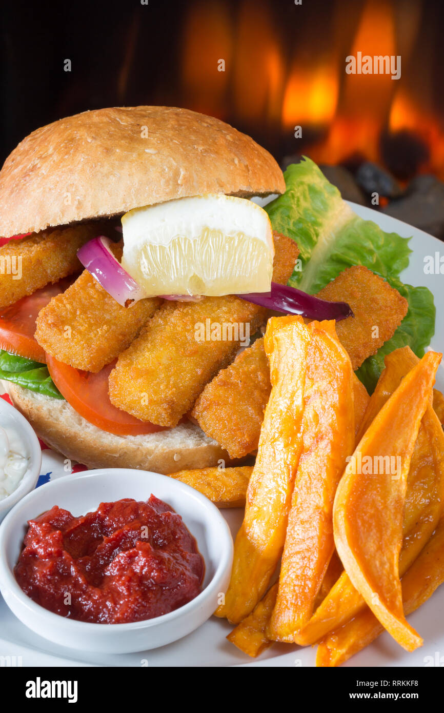 Typical English lunch snack of Fish fingers in a bun, Sweet potato fries, served with ketchup and Tartar. Stock Photo