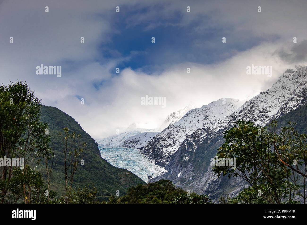Franz Josef Glacier, New Zealand. Retreating glacier with snowy mountain sides, rocky slopes and dark green forest foreground Stock Photo