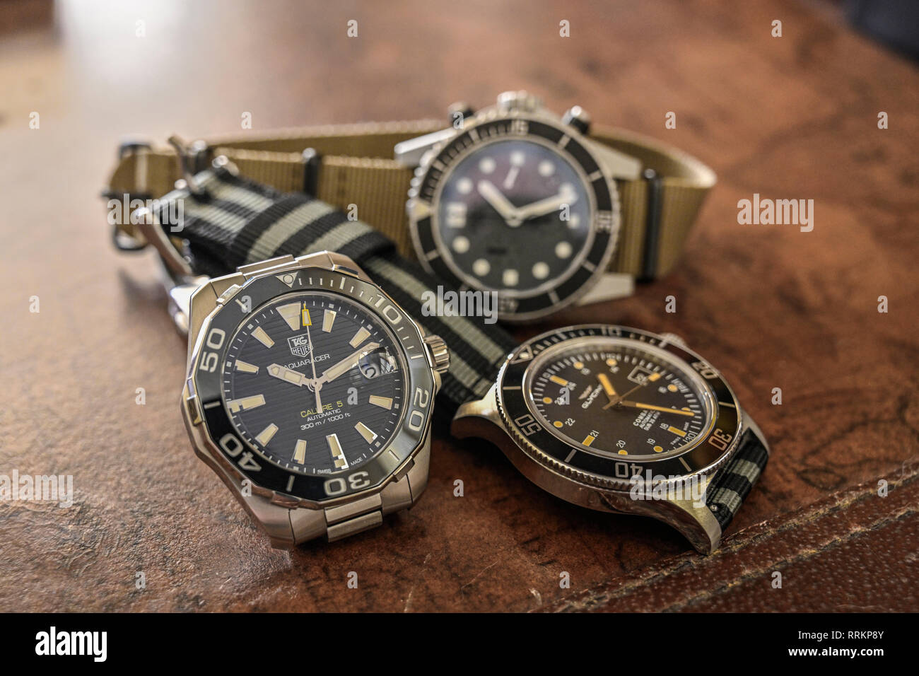 Group of men's luxury diver style wristwatches or timepieces on a dark wood background. Stock Photo