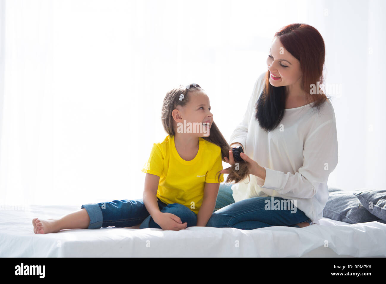 Mom Braids Comb Hair Her Daughter Sitting On The Bed Opposite The 