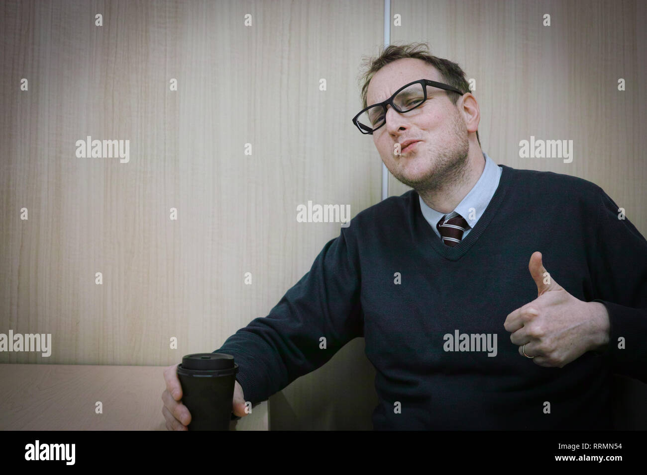 A man at work giving a thumbs up while drinking his coffee. Stock Photo