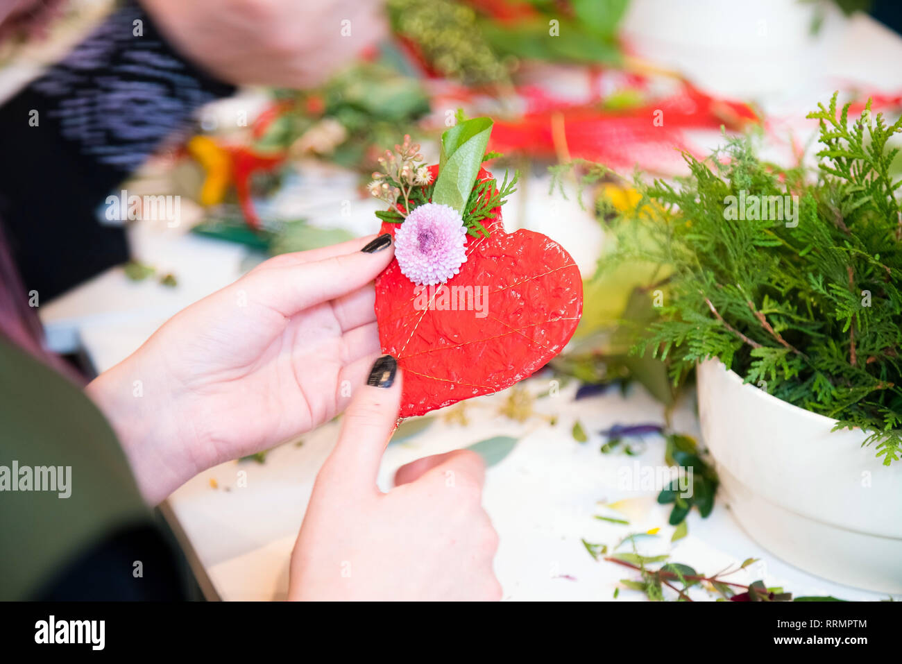 Closeup of hands of young woman florist creating heart shape with flowers bouquet on the table Stock Photo
