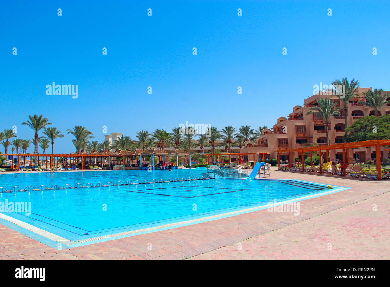 Tropical resort in Egypt. Swimming pool with light blue water palm trees and building of hotel. People rest on Egyptian resort. People enjoy vacations Stock Photo