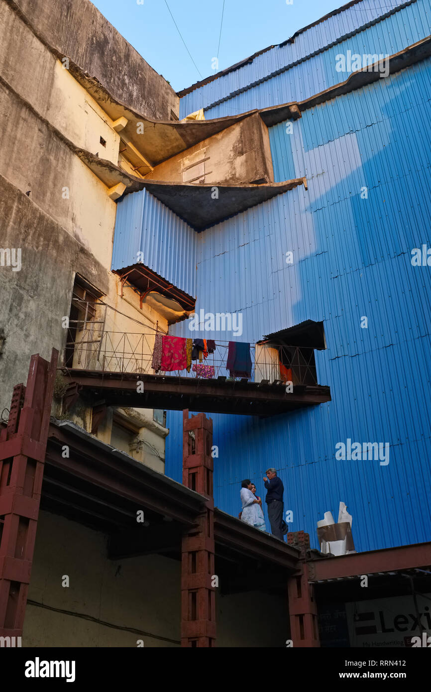 Neighbors in Mumbai, India, having a chat on a makeshift looking skyway at their building, the latter looking rather like a defunct factory Stock Photo